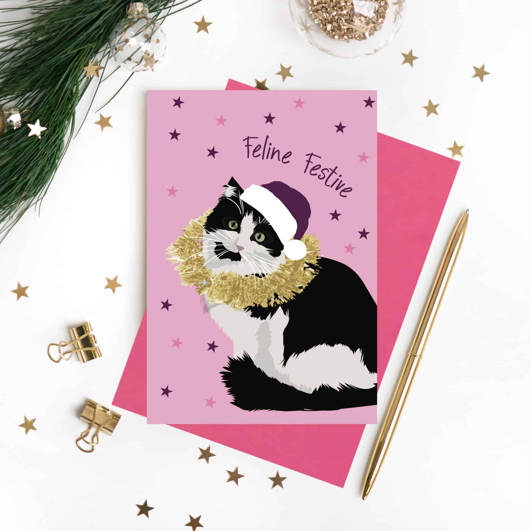 Feline Festive Christmas card featuring a black and white cat wearing a purple Christmas hat and gold-coloured tinsel on pink